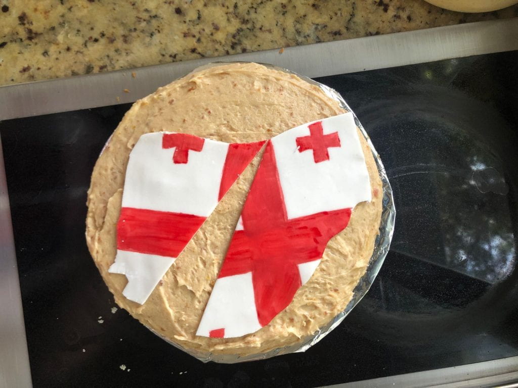 A dissertation cake for Dr. Foley, "Georgian Peach Split Er-gâteau with Date-ive Glaze Marking", prepared by Kelsey Kraus (PhD '18). Almond cake with fresh peach filling and date buttercream, with fondant cutout of the state of Georgia, split, and painted with the flag of the country of Georgia.